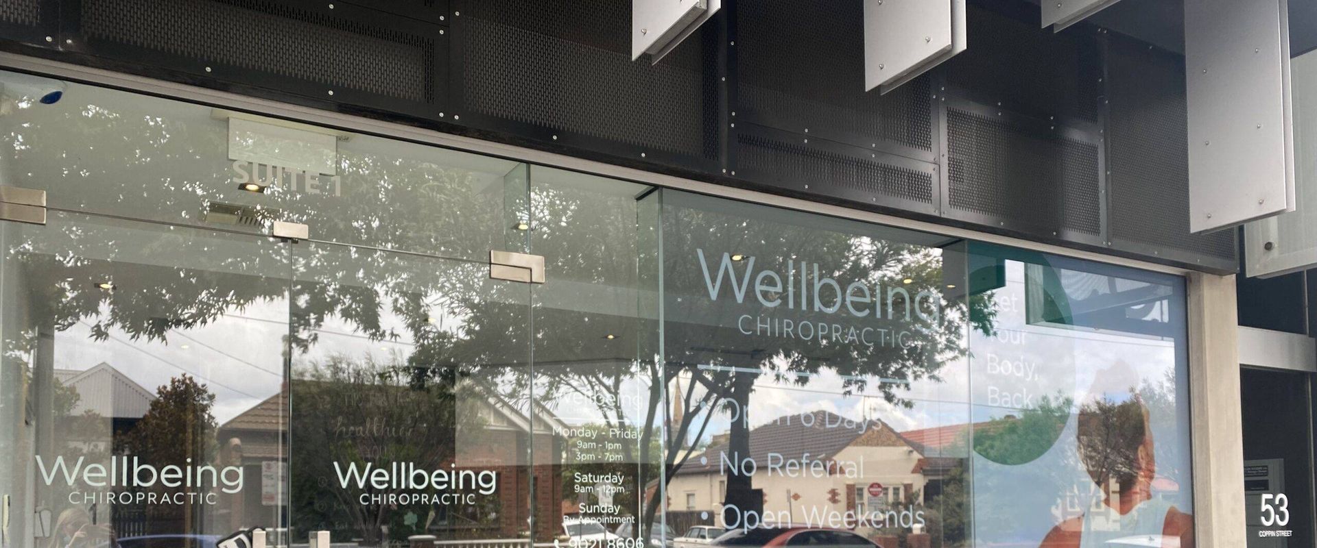 Glass shopfront of a Wellbeing Chiropractic clinic with green window signage
